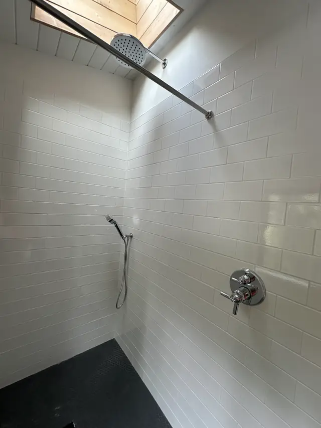 A white subway-tile shower with a rain head and chrome valve plumbed by CSR Plumbing