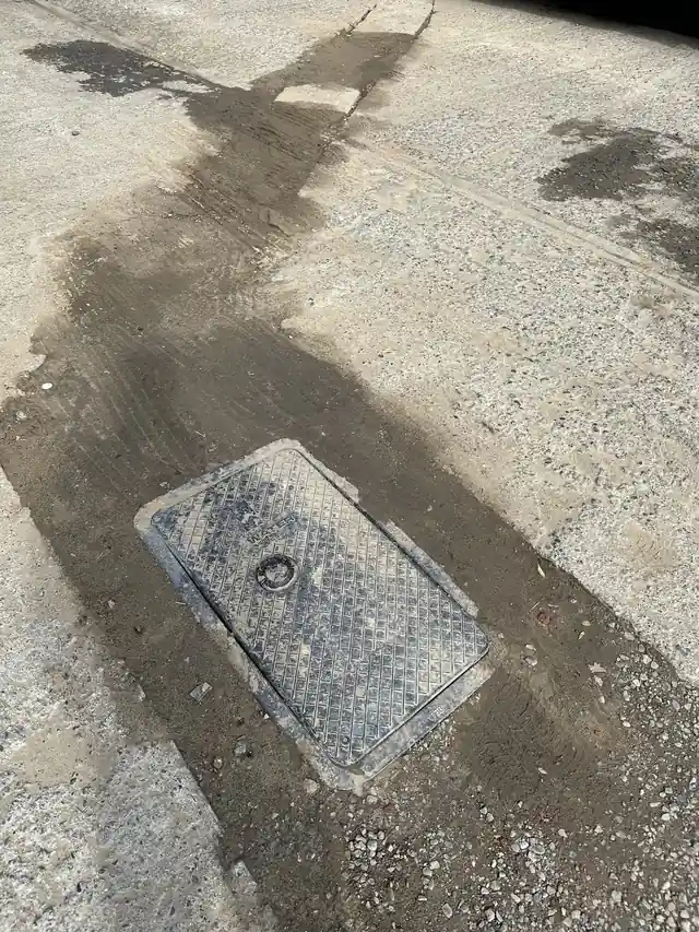 A water meter vault lid and a fresh concrete repair seam after a CSR water-line repair